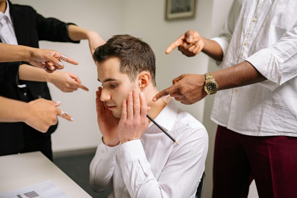 pexels photo 7640415 7640415 A stressed man at the office surrounded by pointing fingers, representing workplace bullying and stress.